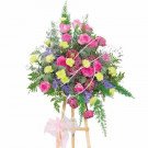 Standing floral arrangement with pink roses, pink lotus flowers, and green carnations.