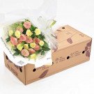 Bouquet of pink and yellow roses with green foliage in a gift box.