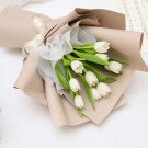 Bouquet of white tulips wrapped in beige paper and white sheer fabric, tied with a cream ribbon.