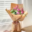 Bouquet of pink lotus flowers and lotus pods wrapped in brown paper with "Romance Flowers" print.