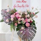A flower arrangement with pink roses, chrysanthemums, and monstera leaves on a white banner.