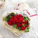 A bouquet of red roses and carnations with greenery, wrapped in newspaper and lace.