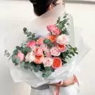 Bouquet of pink and orange roses with eucalyptus leaves, wrapped in white paper.