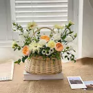 A woven basket overflowing with peach, white, and yellow roses, carnations, and other greenery.