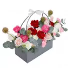 Floral arrangement in a grey rectangular basket with pink, white, and red flowers and green leaves.