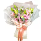 Pink lilies, lisianthus, and delphinium in a bouquet wrapped in sheer paper with a peach bow.