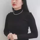 Woman in black turtleneck wearing a pearl necklace and a pearl ring.