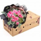 Pink roses and eucalyptus in black and brown wrapping, placed on a cardboard box.