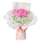 Pink roses and baby's breath bouquet wrapped in light pink paper, tied with a ribbon.