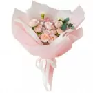 Bouquet of pastel roses, hydrangeas, and carnations wrapped in pink paper with a white ribbon.