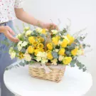 Basket of yellow roses, sunflowers, and carnations with eucalyptus leaves.