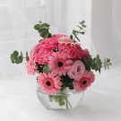 Pink gerbera daisies, carnations, and roses in a clear glass vase with eucalyptus.