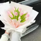 Pink tulips in a white and pink bouquet with a person holding it.