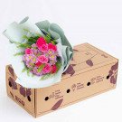 Bouquet of pink roses, carnations, and purple daisies in pastel wrapping, on a floral-stamped cardboard box.