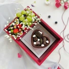 Heart-shaped chocolate pudding with cookies and marshmallows next to a basket of grapes, strawberries, and blueberries.