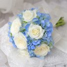 White roses and blue hydrangeas in a bridal bouquet with a lace background.