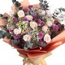 Bouquet of pink and purple roses, hydrangeas, and eucalyptus in peach and cream paper.