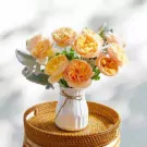 A bouquet of peach and orange roses in a white vase with a jute tie, on a round woven tray.