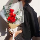 Hand holding a bouquet of red roses with eucalyptus and baby's breath, tied with a white ribbon.
