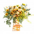 Sunflower arrangement with yellow roses, red berries, and orchids in a basket with orange ribbon.