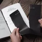 Hands tearing black paper from a book with Vietnamese text.