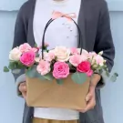 Floral arrangement in a brown paper basket with pink and cream roses, carnations, and greenery.