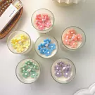 Small glass candles in a gift box, each topped with colorful flower-shaped wax decorations in pink, yellow, blue, peach, mint, and purple.