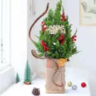 A small evergreen Christmas tree decorated with red berries and a "Merry Christmas" banner in a rustic pot.
