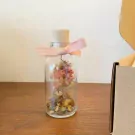 Glass bottle with dried flowers and a pink ribbon on cork stopper, on a wooden surface.