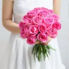 Bride in white dress holding a bouquet of 20 pink roses.