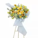 A large, bright floral arrangement with yellow roses, sunflowers, and hydrangeas on a wooden stand.