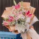 Pink lilies and baby's breath in a brown paper bouquet.