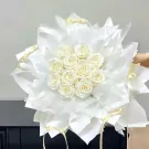 White roses arranged in a bouquet with white wrapping paper and yellow ribbons.