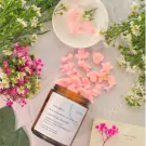 Amber jar of pink wax melts shaped like animals and stars, surrounded by flowers.