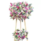 Two-tiered floral arrangement with pink, white, and cream roses, daisies, and other greenery on a wooden stand.