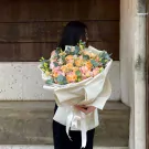 Woman holding a premium bouquet of peach and pink roses with eucalyptus leaves.