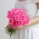 A bride holds a bouquet of 20 bright pink roses.