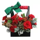 Red roses, carnations, berries, pinecones in a black gift basket with green ribbon.
