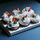 Six mallow cupcakes with white frosting, strawberries, marshmallows, and gold leaf, presented in a white box.