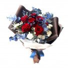 Bouquet of 9 red Ecuador roses, blue accent flowers, and greenery, wrapped in brown and white paper with a blue ribbon.