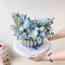 Blue roses and foliage surround a money flower box decorated with rolled banknotes.