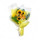 Bouquet of sunflowers, orange carnations, and assorted greens, wrapped in yellow and white paper with a ribbon.
