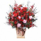 Vase of red roses and pink carnations with eucalyptus leaves, tied with a brown ribbon.
