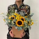 A woman holds a basket arrangement of sunflowers and daisies.