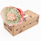 A flower bouquet with a smiling pink flower and baby's breath sits on a delivery box.