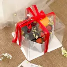 Clear gift box with red ribbon holding strawberries, grapes, orange, and flowers.