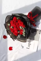 Red roses in a black bouquet with a red ribbon, next to a magazine on a white surface.