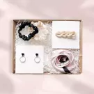 Gift box with scrunchies, earrings, hairpin, and scarf in neutral colors.