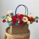 Brown flower bag with red roses, pink and yellow gerbera daisies, and eucalyptus leaves.
