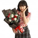 Young woman with a bouquet of red and white roses, eucalyptus, and purple flowers, wrapped in black paper with a red ribbon.